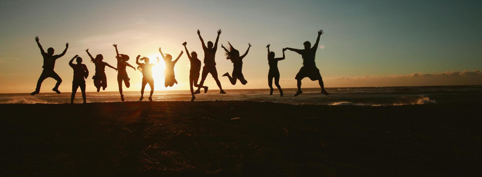 people at the beach jumping for joy at sunset